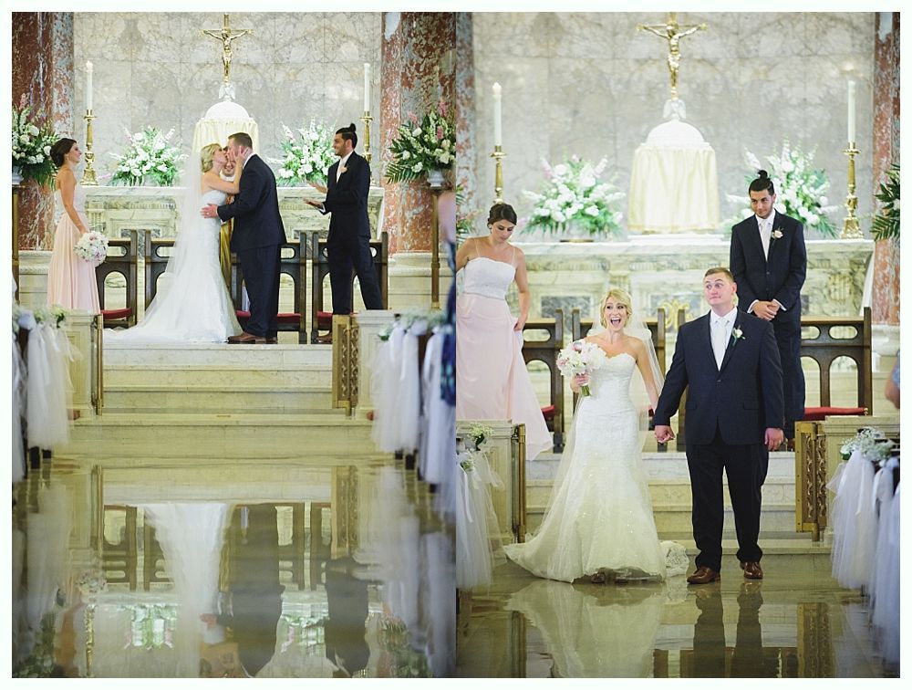 Bride with arms up, making a funny face, groom looking at his hand, cake cutting in background.