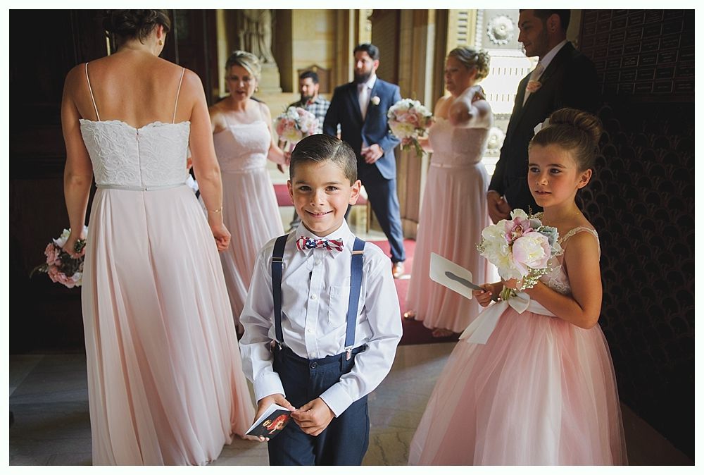 Bride with arms up, making a funny face, groom looking at his hand, cake cutting in background.