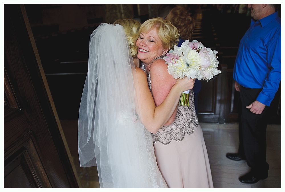 Bride with arms up, making a funny face, groom looking at his hand, cake cutting in background.