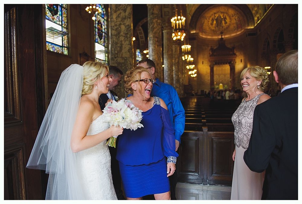 Bride with arms up, making a funny face, groom looking at his hand, cake cutting in background.