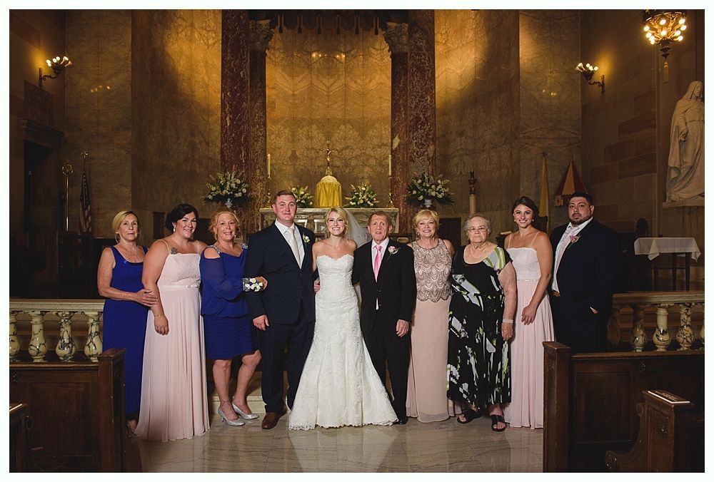 Bride with arms up, making a funny face, groom looking at his hand, cake cutting in background.