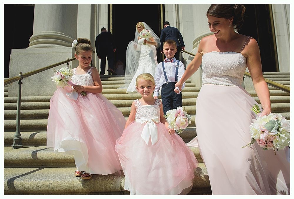 Bride with arms up, making a funny face, groom looking at his hand, cake cutting in background.