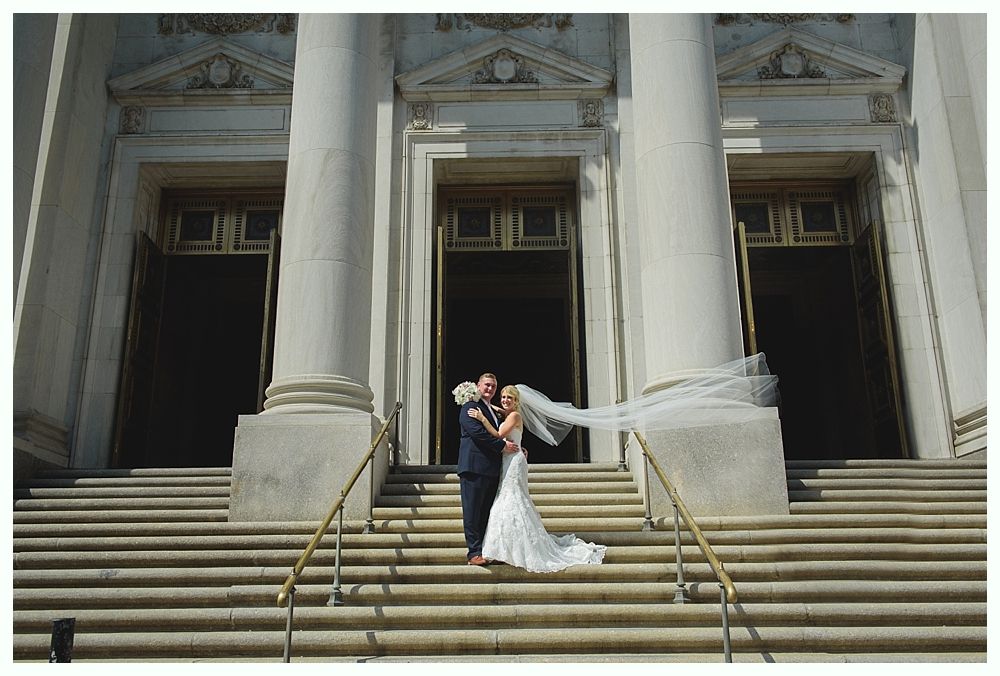 Bride with arms up, making a funny face, groom looking at his hand, cake cutting in background.