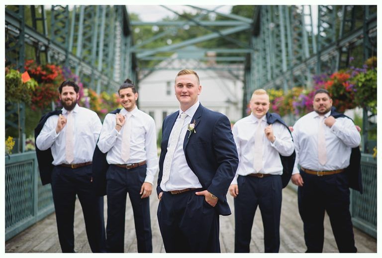 Bride with arms up, making a funny face, groom looking at his hand, cake cutting in background.