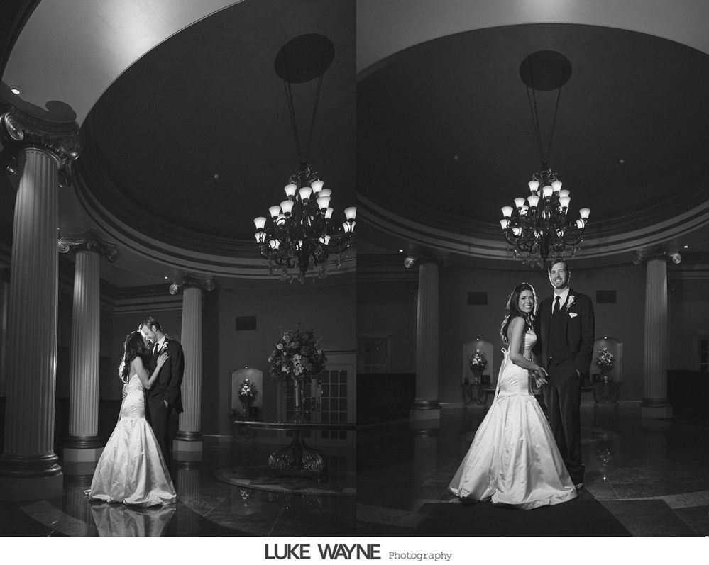Wedding couple in elegant ballroom with chandeliers and columns.