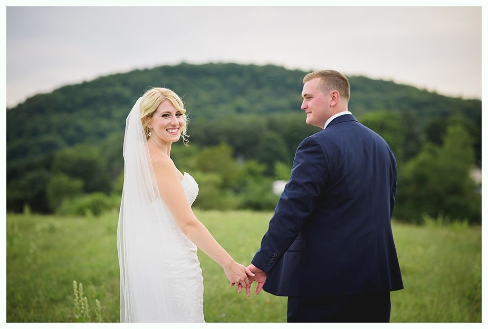 Bride with arms up, making a funny face, groom looking at his hand, cake cutting in background.