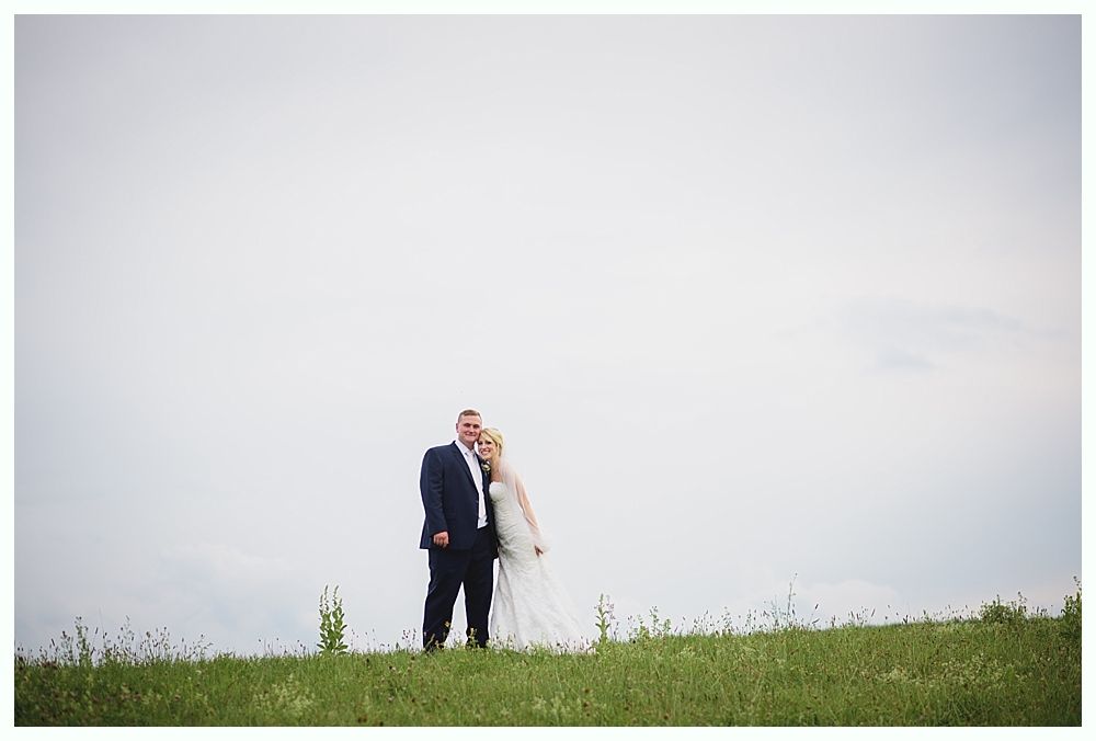 Bride with arms up, making a funny face, groom looking at his hand, cake cutting in background.