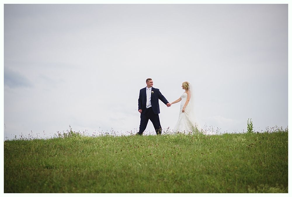 Bride with arms up, making a funny face, groom looking at his hand, cake cutting in background.