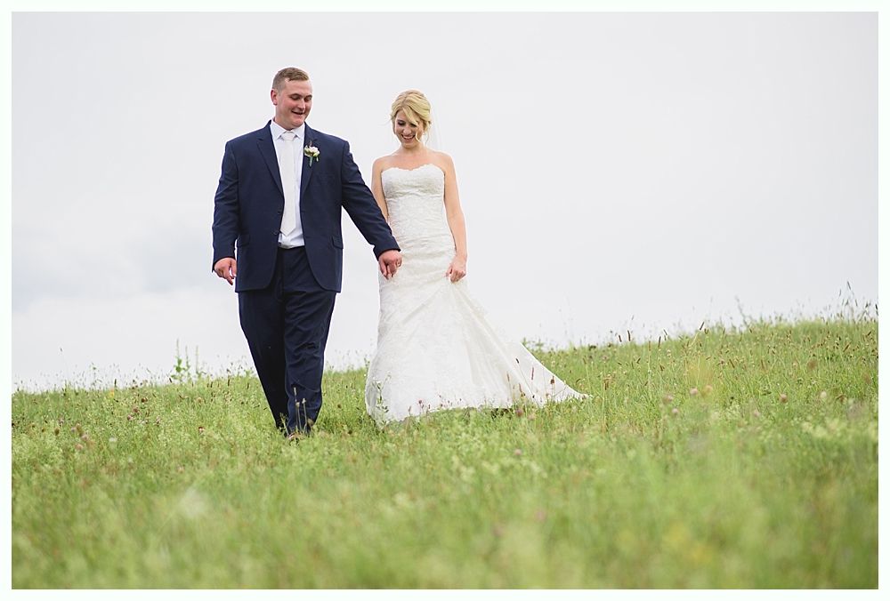 Bride with arms up, making a funny face, groom looking at his hand, cake cutting in background.