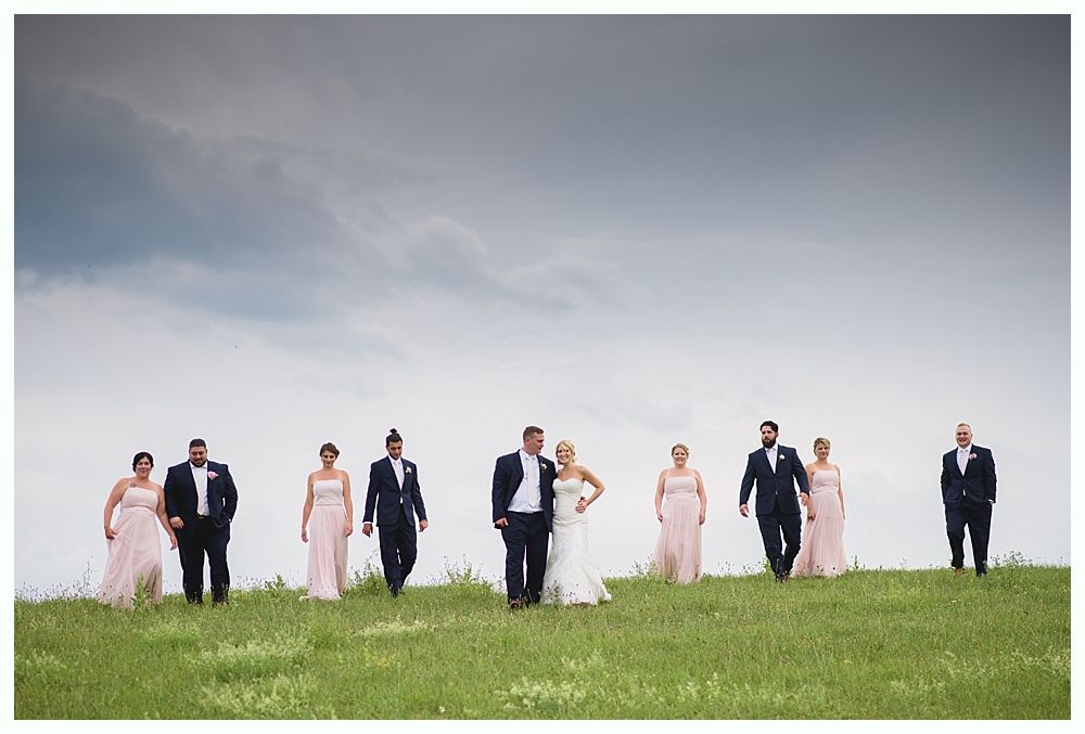 Bride with arms up, making a funny face, groom looking at his hand, cake cutting in background.