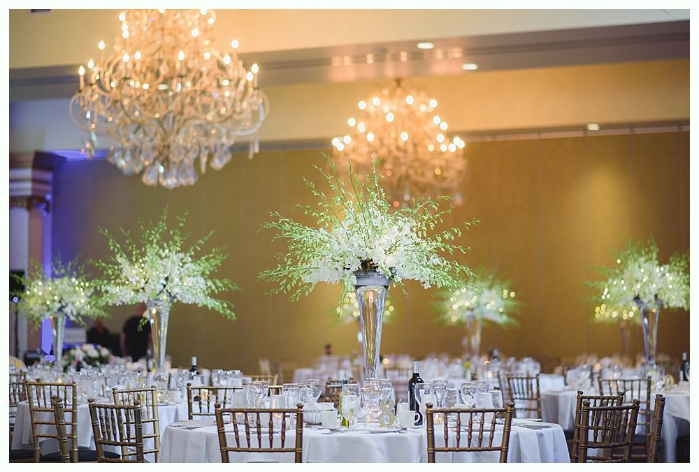 Bride with arms up, making a funny face, groom looking at his hand, cake cutting in background.