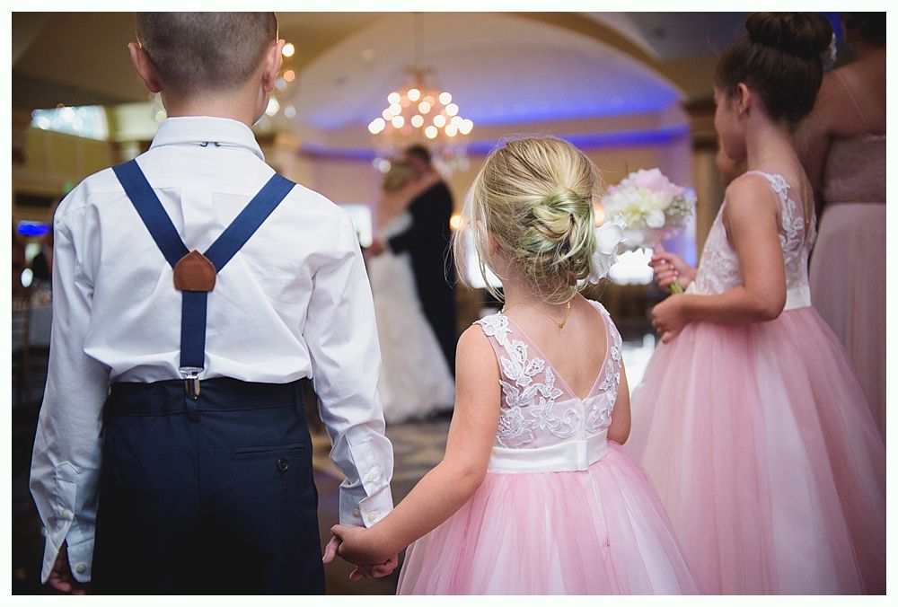 Bride with arms up, making a funny face, groom looking at his hand, cake cutting in background.