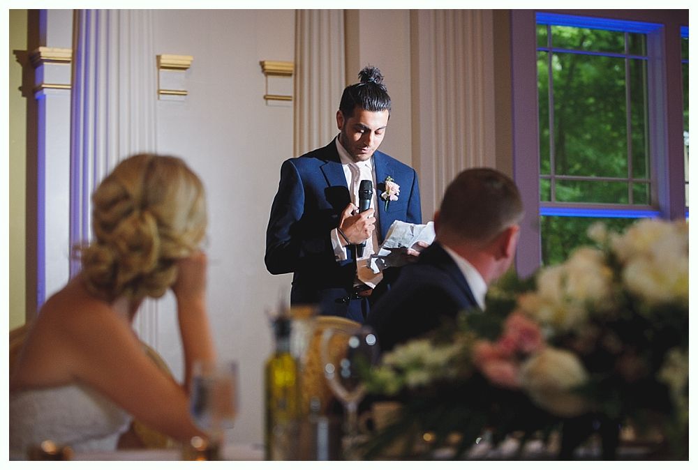 Bride with arms up, making a funny face, groom looking at his hand, cake cutting in background.