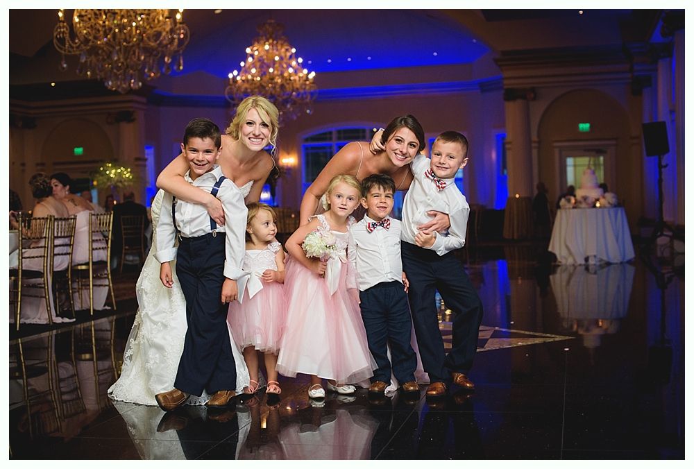 Bride with arms up, making a funny face, groom looking at his hand, cake cutting in background.