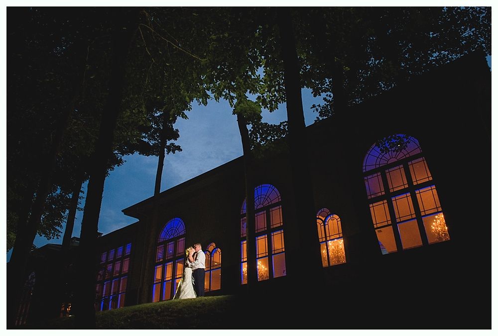 Bride with arms up, making a funny face, groom looking at his hand, cake cutting in background.