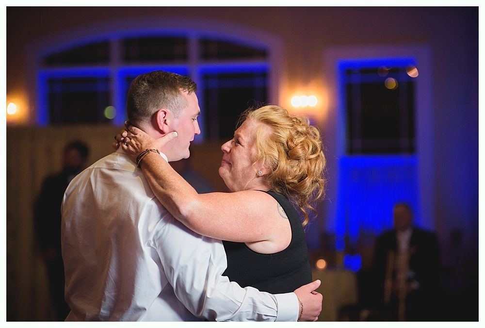 Bride with arms up, making a funny face, groom looking at his hand, cake cutting in background.