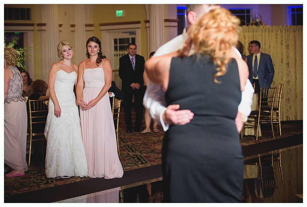 Bride with arms up, making a funny face, groom looking at his hand, cake cutting in background.