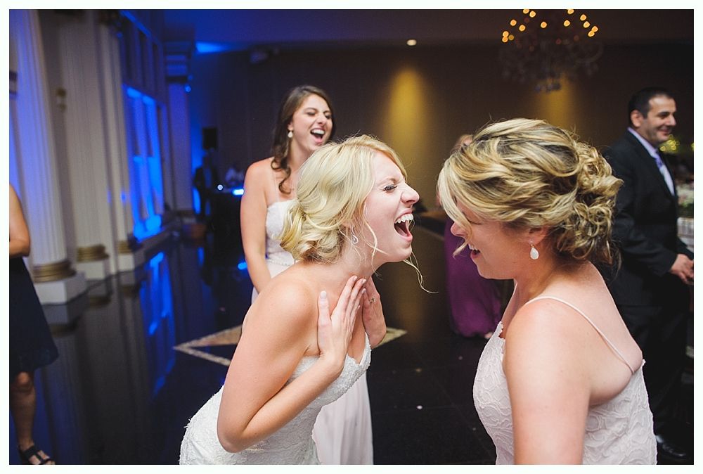 Bride with arms up, making a funny face, groom looking at his hand, cake cutting in background.