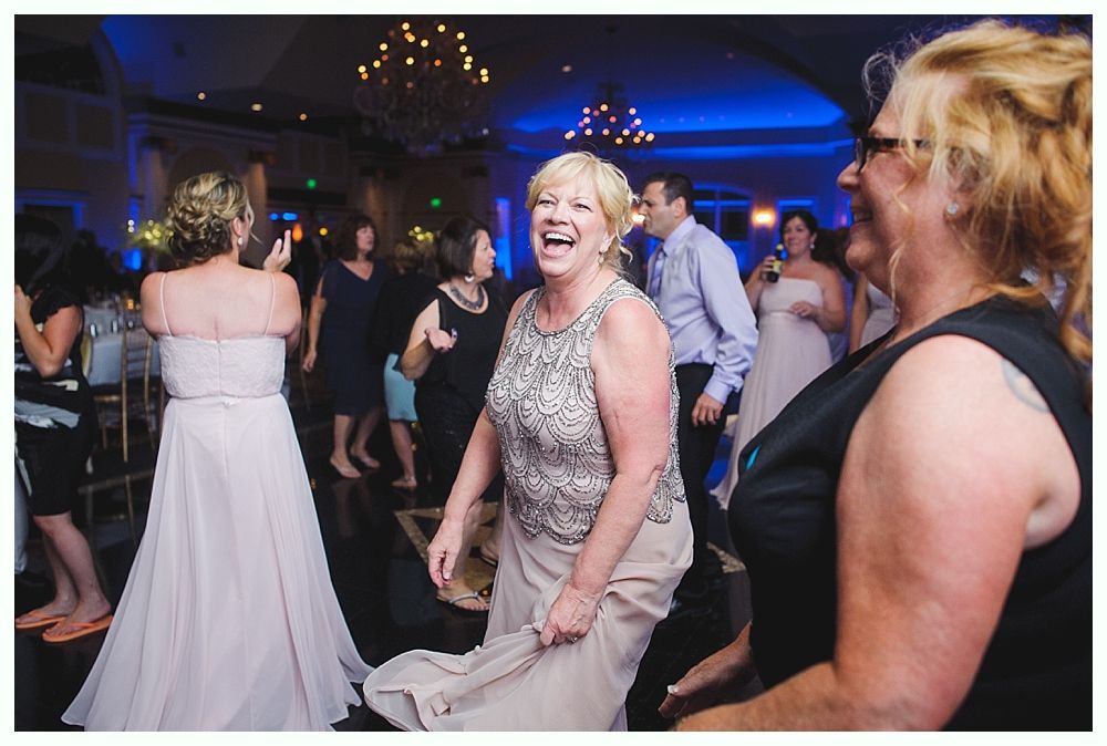 Bride with arms up, making a funny face, groom looking at his hand, cake cutting in background.