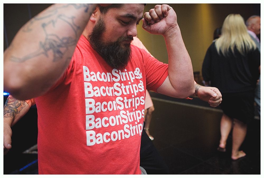Bride with arms up, making a funny face, groom looking at his hand, cake cutting in background.