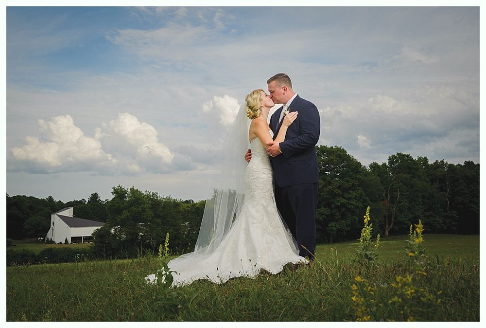 Couple on boardwalk by ocean, framed by beach plants under a blue sky with clouds.