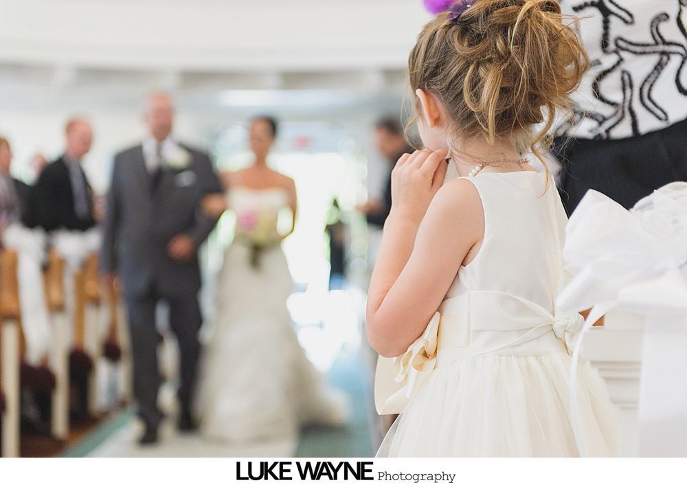 Couple kissing at their wedding ceremony inside a glass-roofed structure, surrounded by guests.