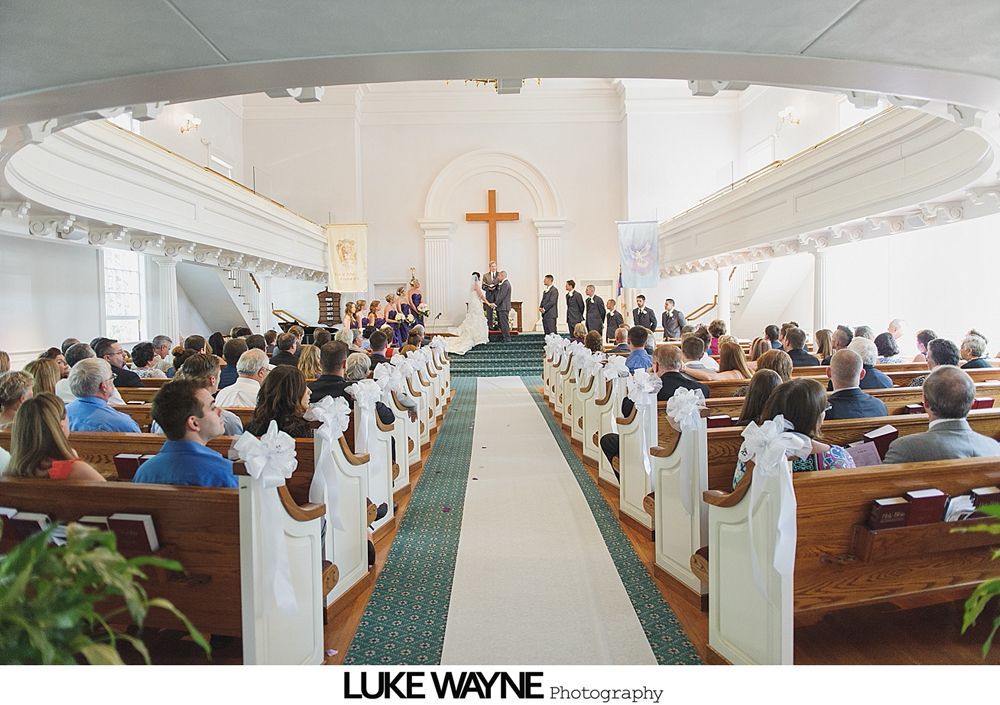 Wedding party posing on a rural road; bride and bridesmaids in pastel dresses, groomsmen in gray suits.