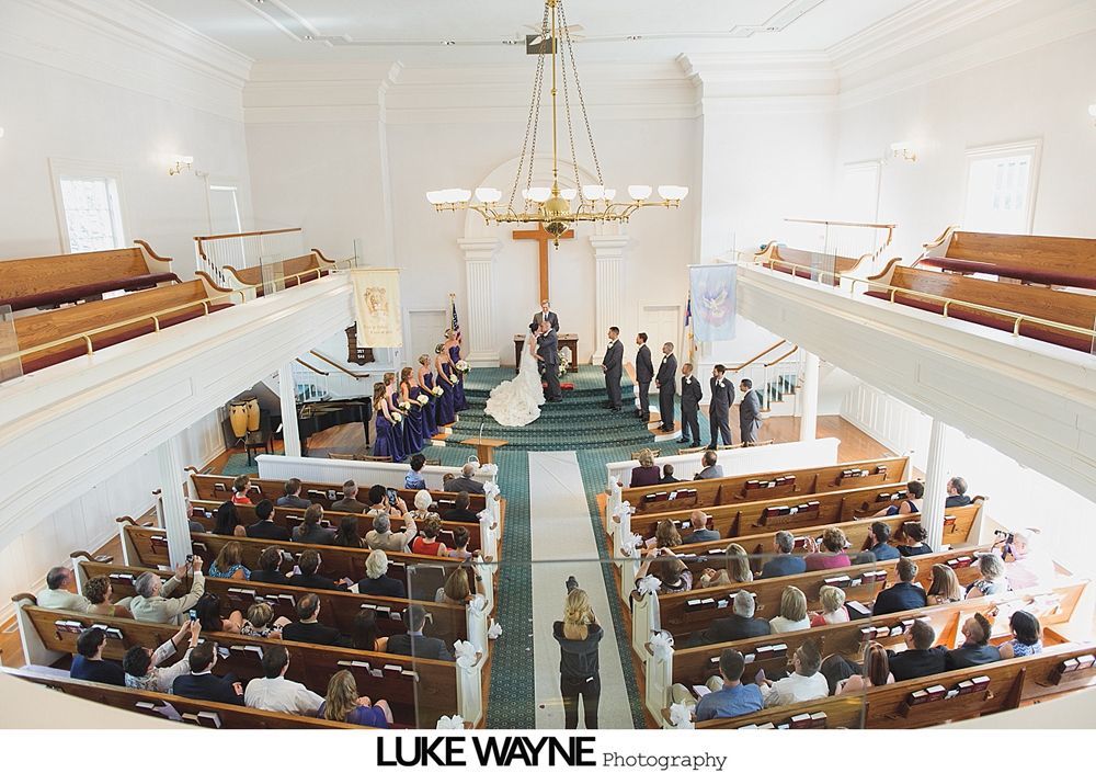 Wedding party posing in a field. People in formal wear with bouquets, smiling. Green field, cloudy sky.
