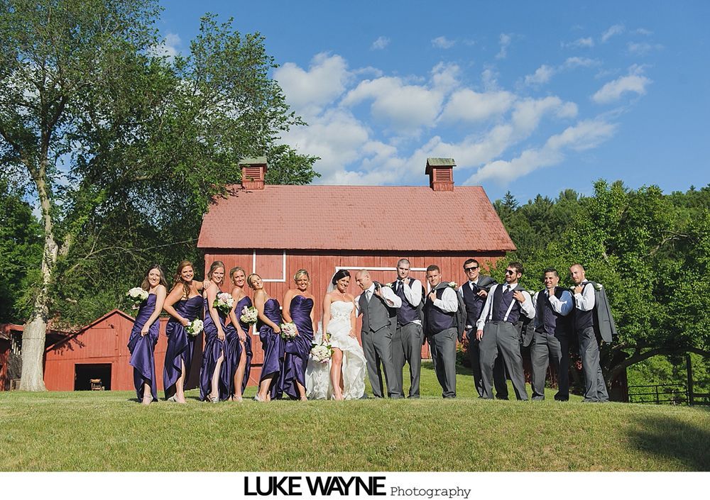 Bride and groom embrace on a country road, laughing, with green field and trees in the background.