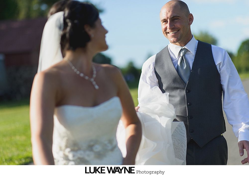 Wedding couple embracing on a rural road; the bride wears a white dress and veil, the groom in a suit and vest.