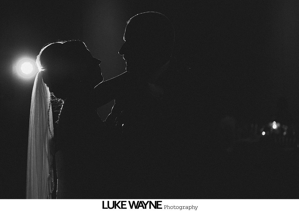 Wedding couple kissing under an umbrella in the rain.