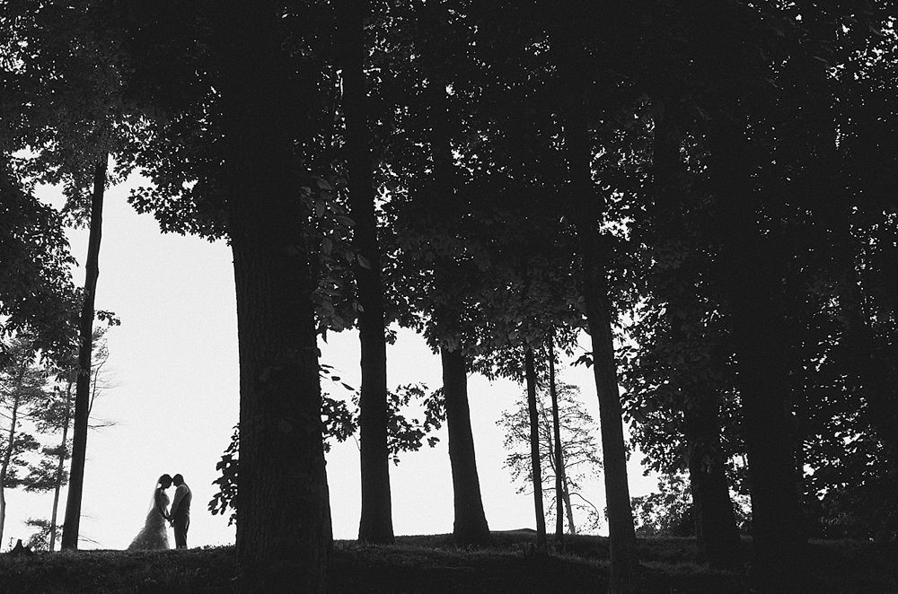 Group photo at a wedding reception. Bride and groom centered, surrounded by guests in formal attire.