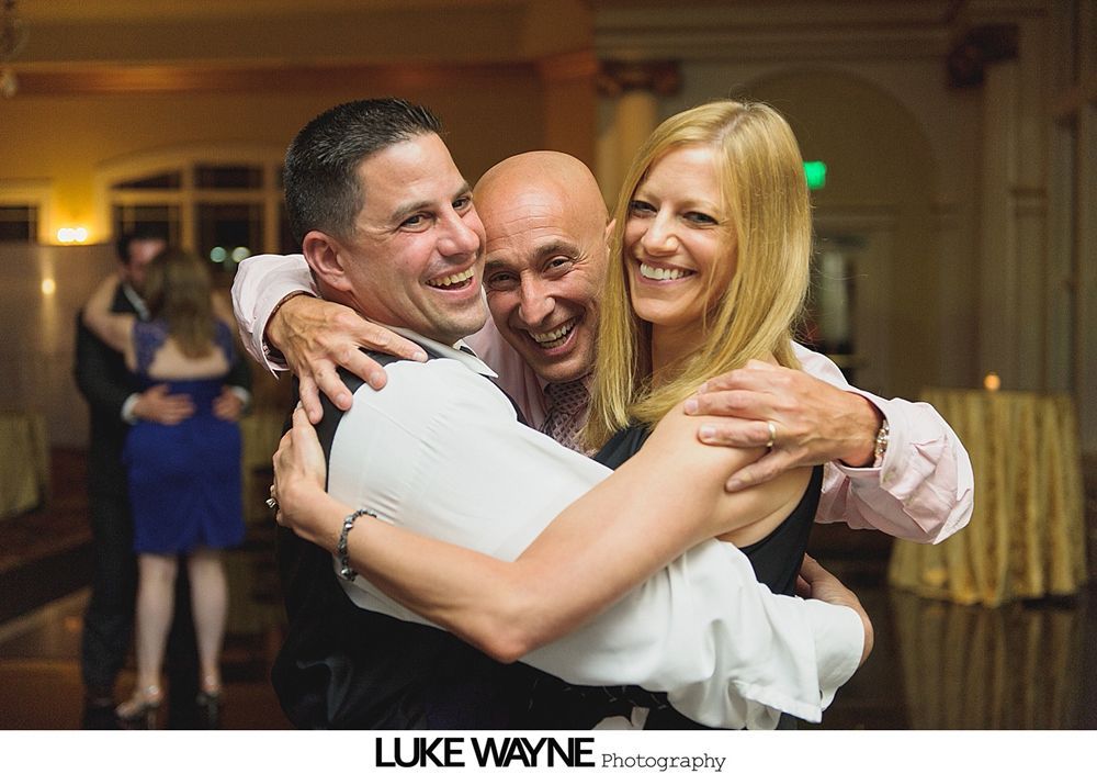 Group photo at a wedding reception. Bride and groom centered, surrounded by guests in formal attire.