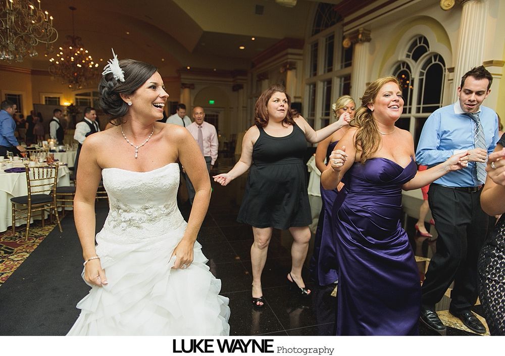 Group photo at a wedding reception. Bride and groom centered, surrounded by guests in formal attire.