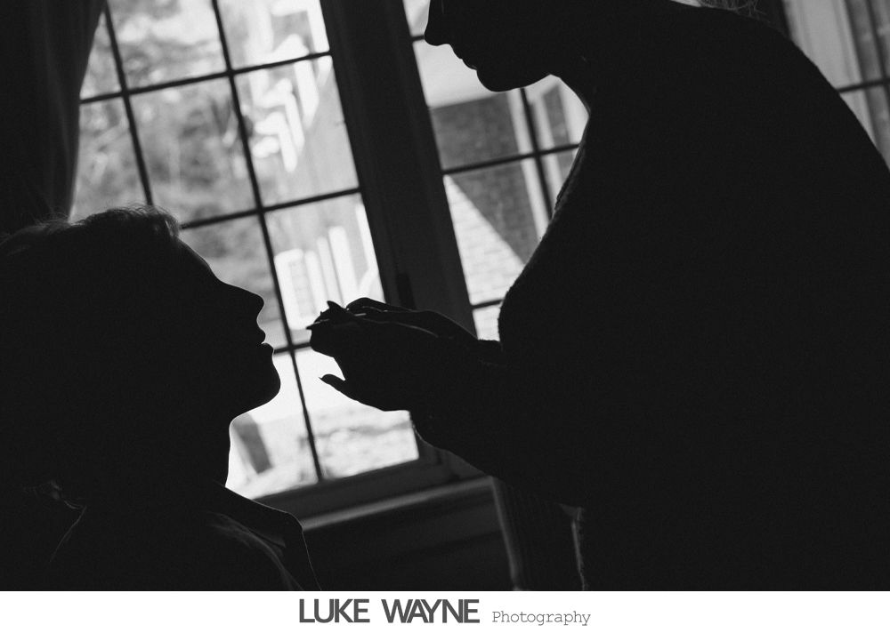 Silhouette of someone applying makeup near a window, natural light.