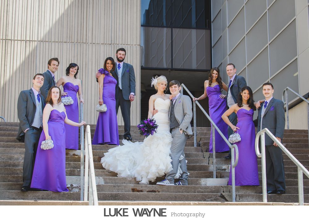 Wedding party on steps, bride in white dress, bridesmaids in purple dresses, groomsmen in gray suits.