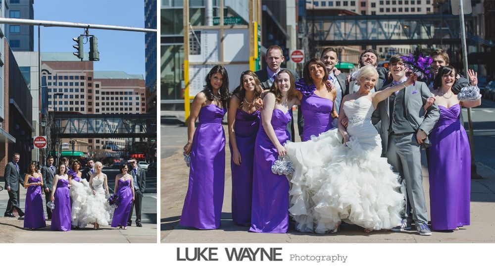 Wedding party in purple and gray outfits posing outdoors in front of city buildings.