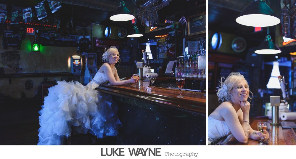 Bride in a fluffy white dress at a bar, smiling. Dark interior, fluorescent lights.