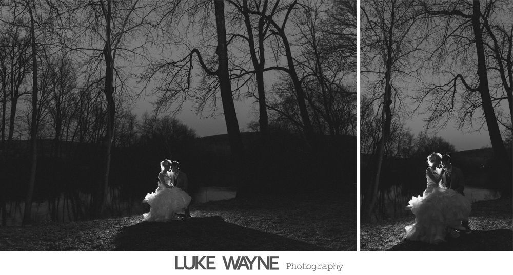 Bride in wedding dress, seated outdoors at dusk, with bare trees in the background. Black and white photo.