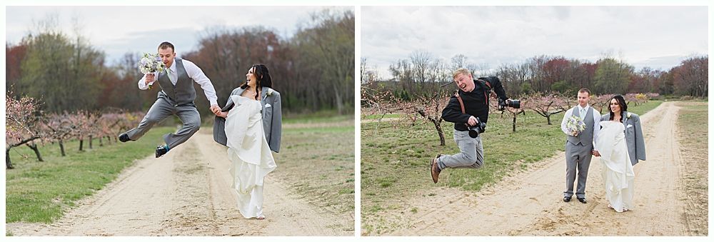 Wedding couple and photographer jumping on a dirt path in an orchard. Overcast sky.