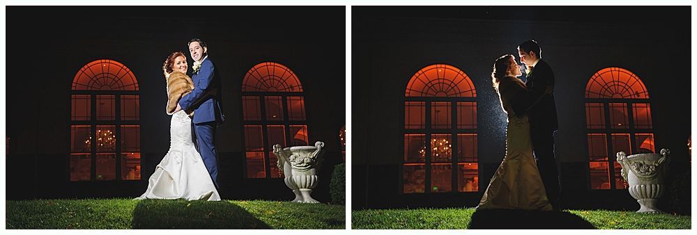 A couple embraces outdoors at night, lit by spotlights. They stand in front of large arched windows and garden.