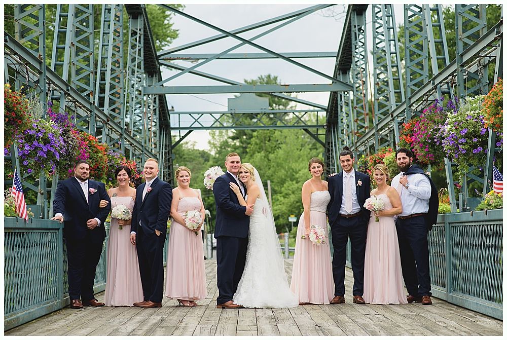 Wedding party on a green bridge, bride and groom in the center, bridesmaids in pink, groomsmen in navy.