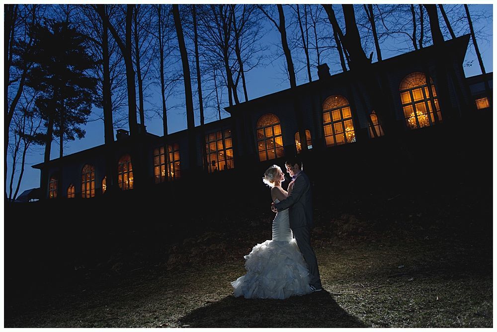 Couple embraces in front of a building with lit windows at night.