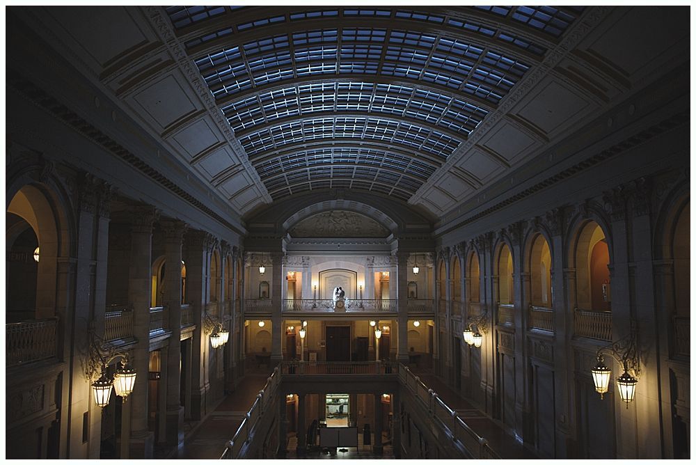 Ornate interior of a building with a glass ceiling. Columns and archways line the walls.