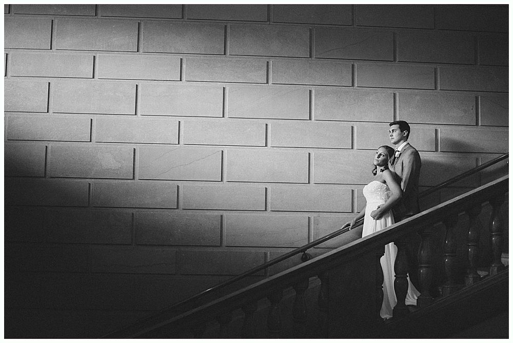 Couple standing on stairs, illuminated by a light source against a textured wall.