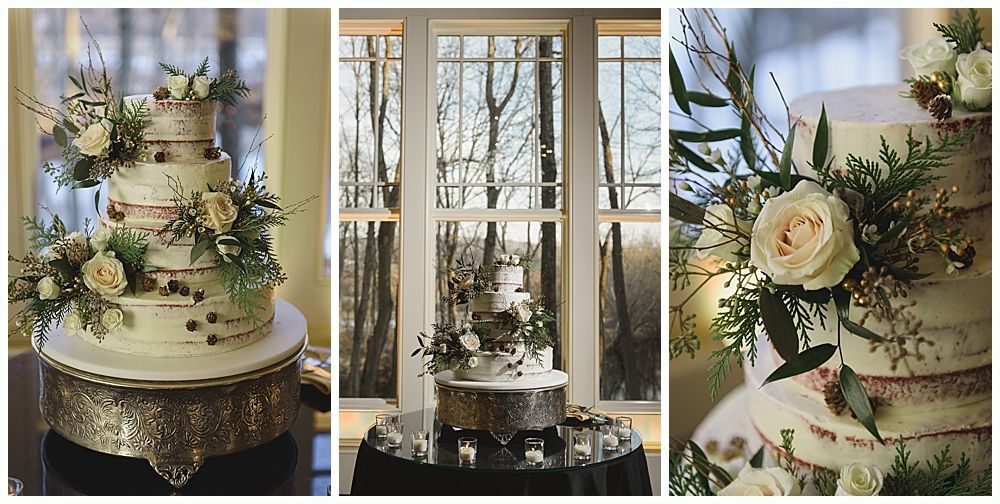 Three-tiered wedding cake, decorated with flowers and greenery, in front of a window overlooking bare trees.