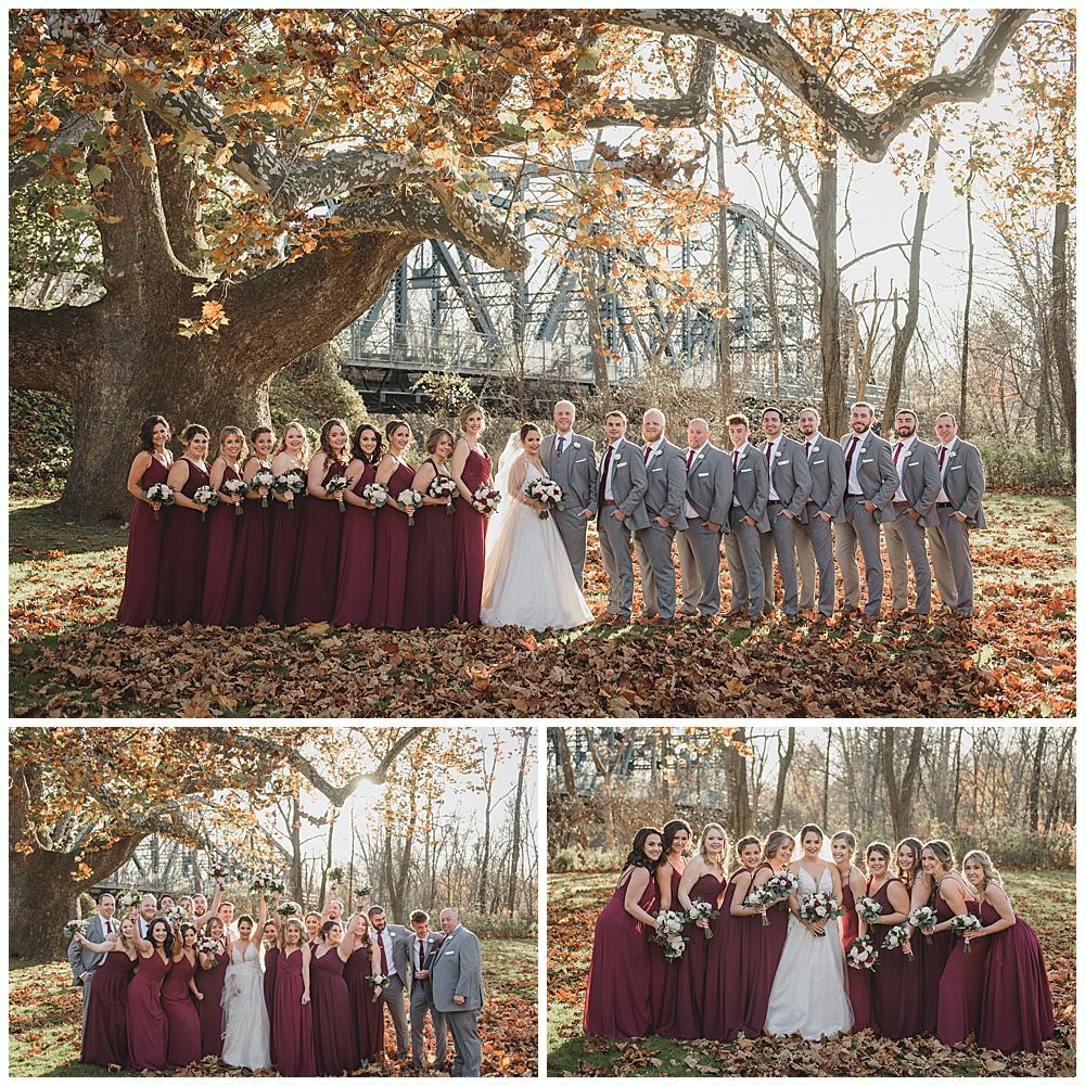 Wedding party posing outdoors; bride, bridesmaids in burgundy, groomsmen in gray, autumn leaves.