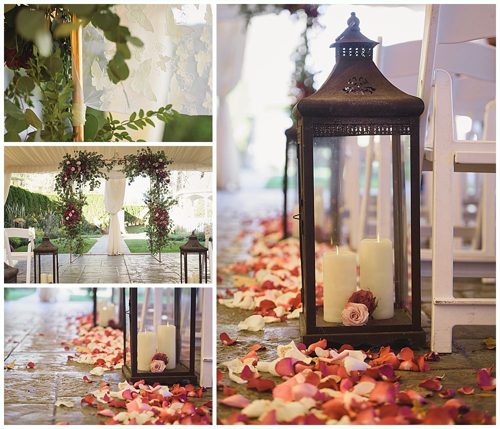 Wedding ceremony setup: lanterns with candles, rose petals, floral arch, and white chairs.
