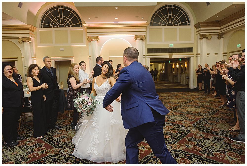 Bride and groom dancing, cheered on by wedding guests in a ballroom.