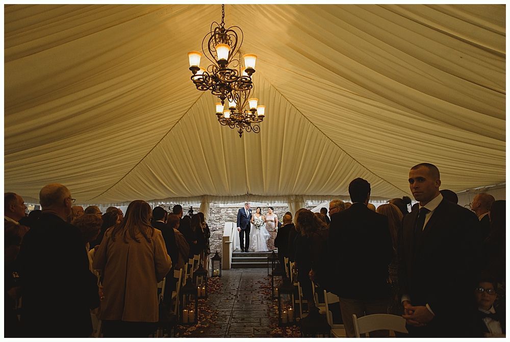 Wedding ceremony under a tent with guests, couple, and officiant.